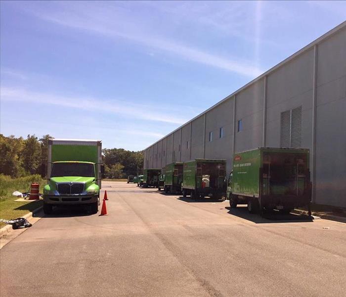 Several green SERVPRO trucks parked outside a large commercial facility.